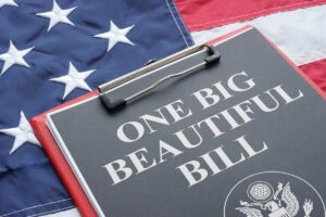 A clipboard with a black piece of paper that says “ONE BIG BEAUTIFUL BILL” on top of an American flag.